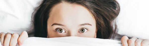 Frau schaut unter ihrer Bettdecke hervor