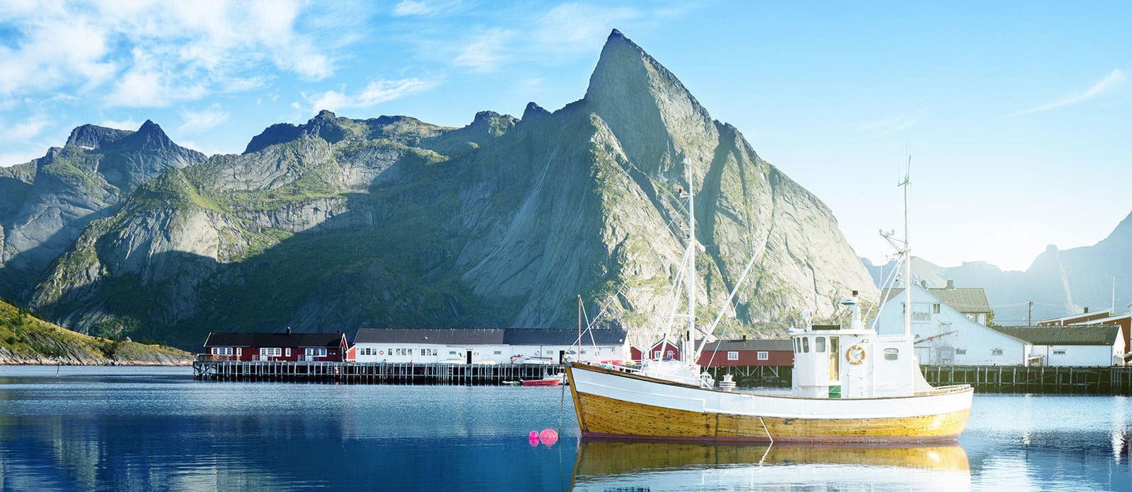Fischerdorf mit Booten an der norwegischen Küste vor schneebedeckten Bergen