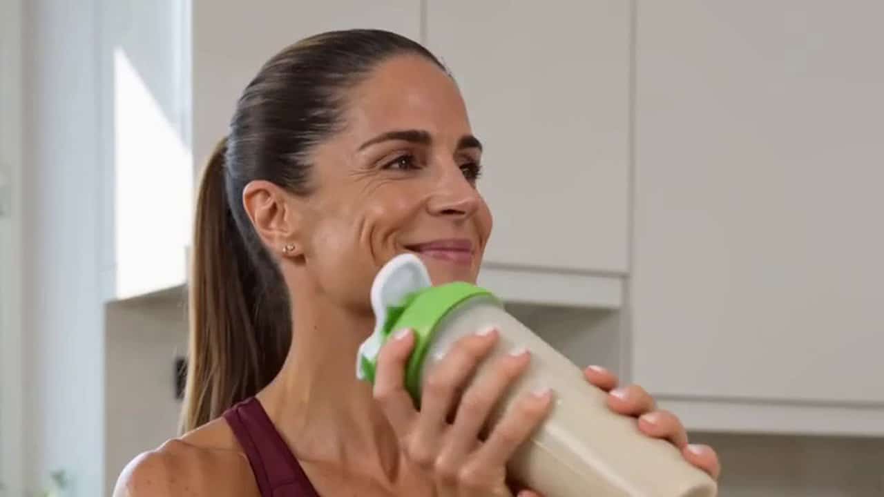 Frau trinkt einen veganen Proteinshake aus dem Shaker in der Küche